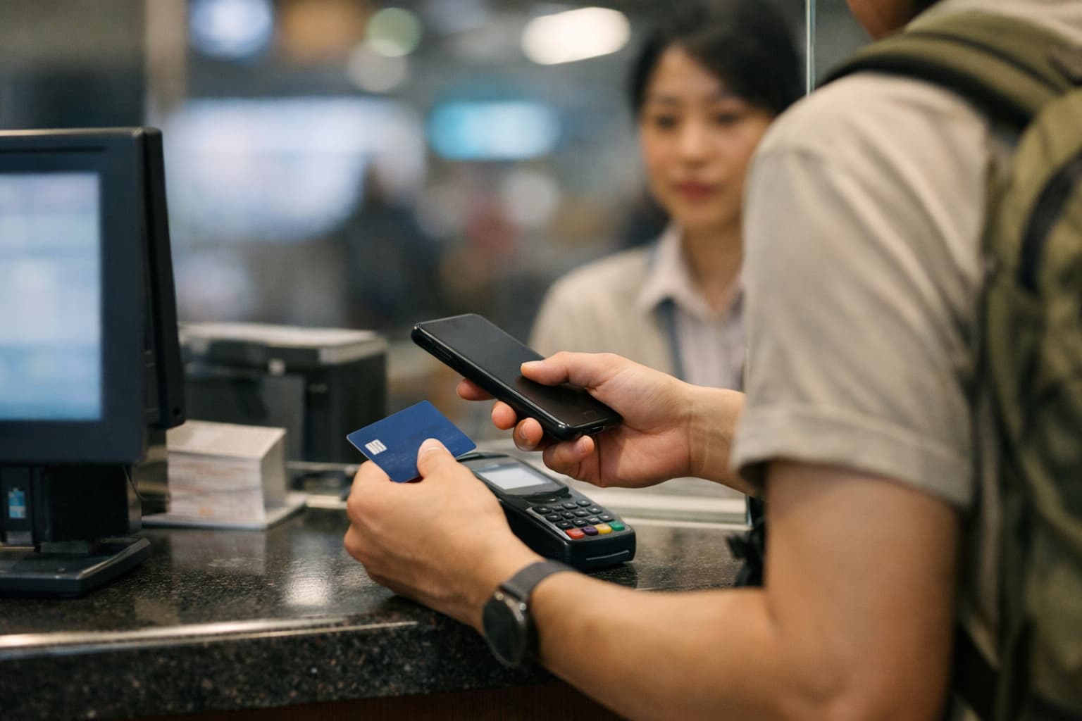 Traveler at a station kiosk with card and phone in a subtle payment-friction moment.